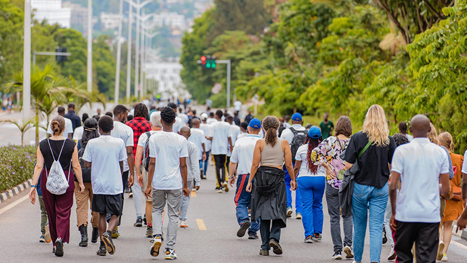 a group of people walking through a car free, tree-lined street in kigali