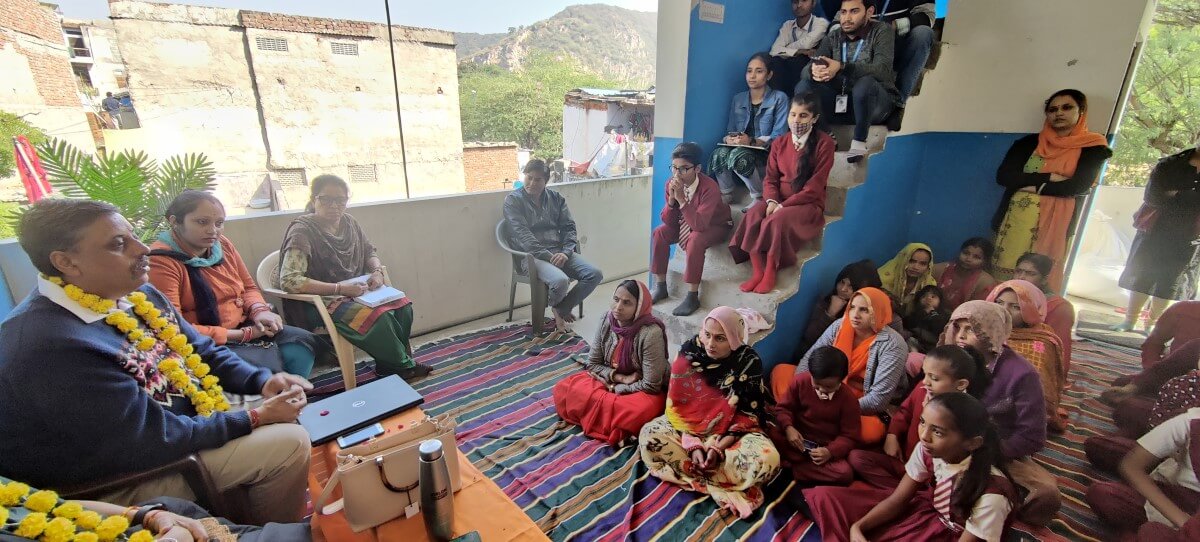 A photograph of a stakeholder meeting. Several people are gathered in a room, and buildings and mountains are visible in the background.