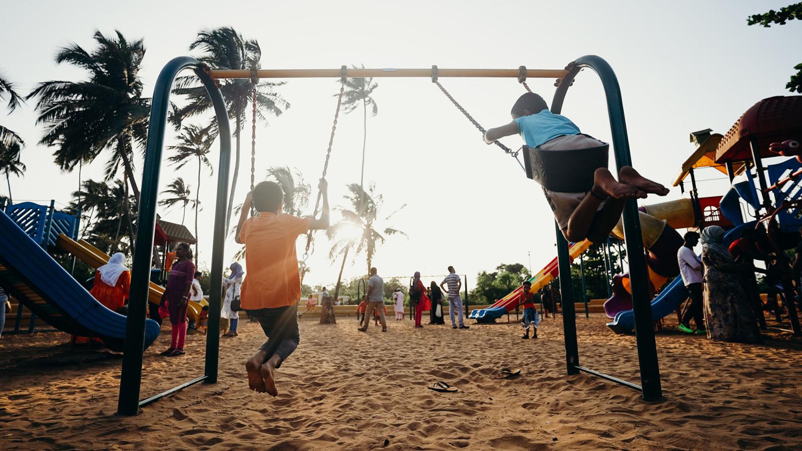 children on a swingset at sunset with palm trees in the background