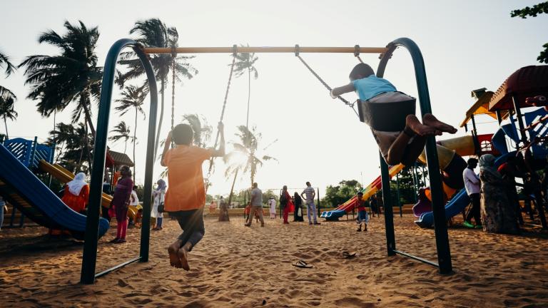 Children playing on swings in a neighborhood park lined with trees