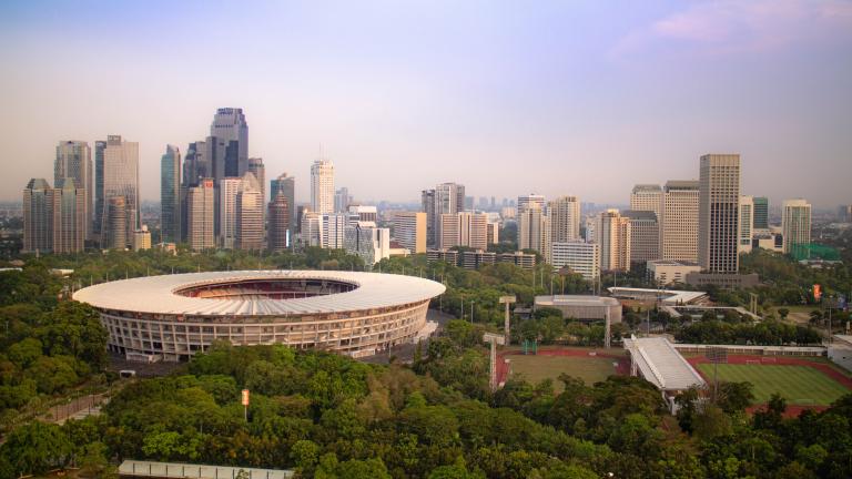 A view of Gelora Bung Karno Stadium in Jakarta surrounded by trees and the city skyline