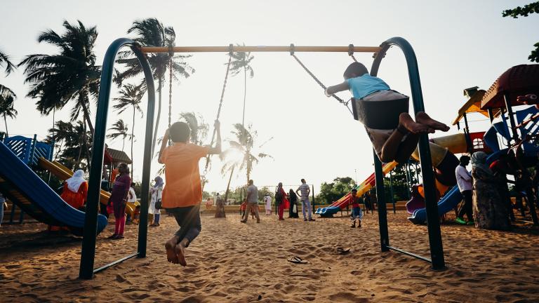 children on a swingset at sunset with palm trees in the background