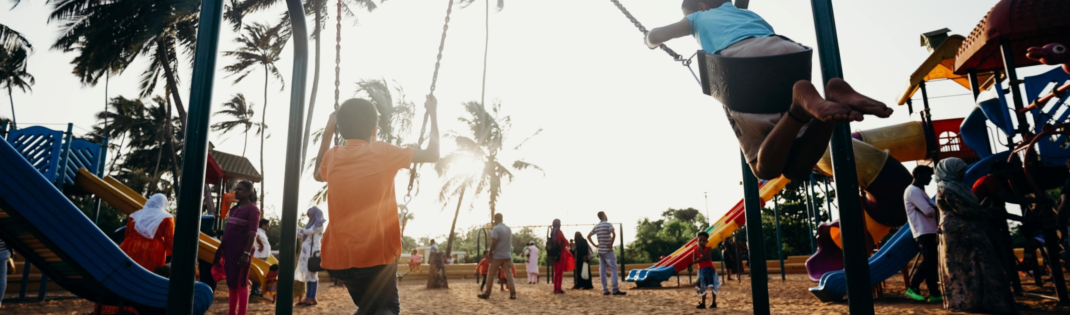 Children playing on swings in a neighborhood park lined with trees
